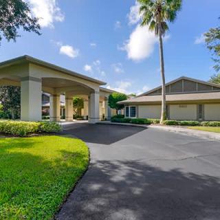 A modern residential building with a covered driveway, surrounded by well-maintained landscaping and a tall palm tree on a bright sunny day.