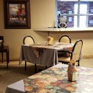A cozy restaurant interior with tables and chairs, decorated with floral tablecloths and a painting on the wall.