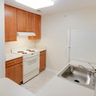 A simple kitchen interior with wooden cabinets, a stove, and a sink.