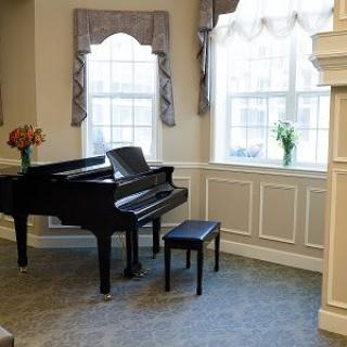 A grand piano in a well-lit living room with large windows and floral decorations.