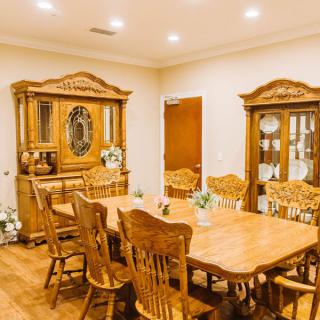 A traditional dining room with wooden furniture featuring a large table and chairs, illuminated by ceiling lights.