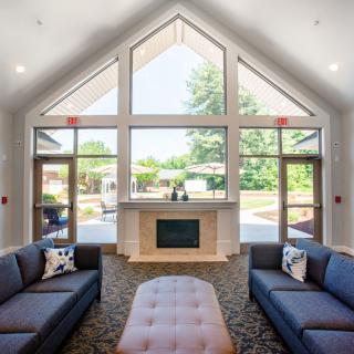 A modern living room with high ceilings, large windows, and a central fireplace.