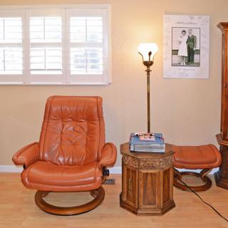 A cozy living room setup featuring a leather chair, side table with books, and a floor lamp next to a window.