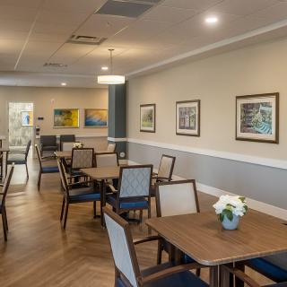 A well-designed dining area with wooden tables and chairs, decorated with artwork and flowers.