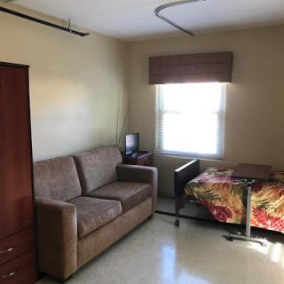 A cozy room featuring a couch and a neatly made bed, illuminated by natural light from the window.