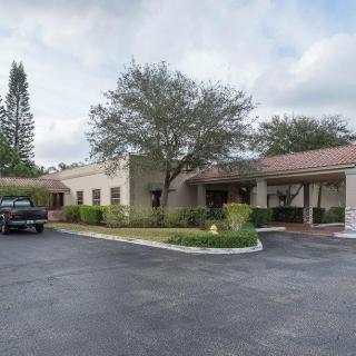 A single-story building with a parking lot and trees on a cloudy day.