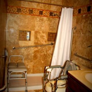 A wheelchair-accessible bathroom featuring a shower chair and grab bars, designed for ease of use.