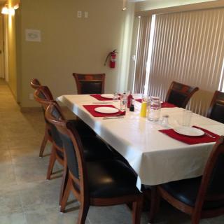 A dining room with a table set for a meal, featuring red and white place settings and wooden chairs.
