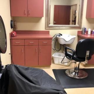 A hair salon interior featuring a styling chair, a sink for washing hair, and cabinets for storage.