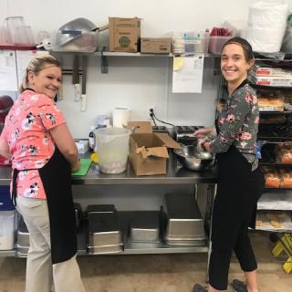 Two women smiling while preparing food in a kitchen.