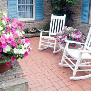 A charming patio with white rocking chairs and vibrant flowers, perfect for relaxation.
