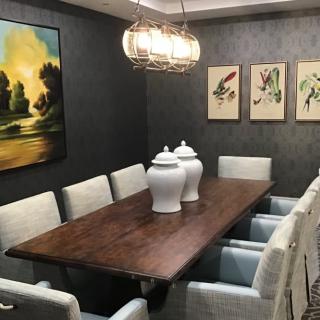 A modern dining room with a wooden table, upholstered chairs, decorative jars, and framed artwork.