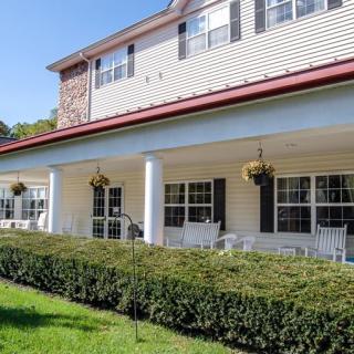 A two-story house with a porch, featuring rocking chairs and hanging plants, surrounded by well-maintained hedges on a sunny day.