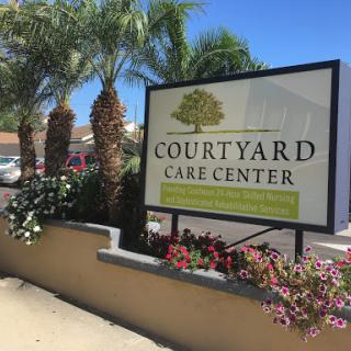 The Courtyard Care Center sign surrounded by lush greenery and flowers.