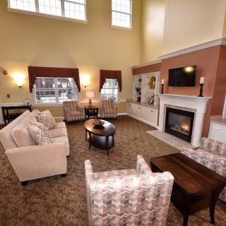 A cozy living room with a high ceiling, featuring plush seating arrangements around a central coffee table and a fireplace.
