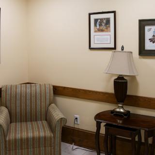 A cozy waiting area featuring a striped armchair, a side table with a lamp, and framed pictures on the walls.