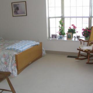 A cozy bedroom featuring a bed, a rocking chair, and some potted plants by the window.