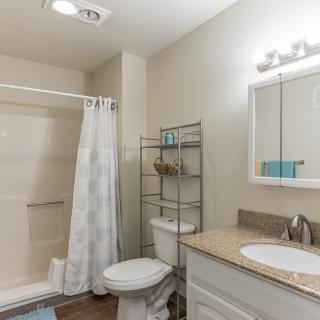 A modern bathroom with a shower, toilet, and sink, featuring a mirror and storage rack.
