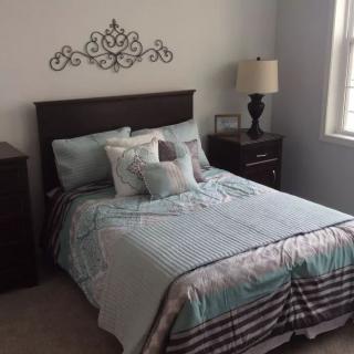 A neatly made bed with decorative pillows in a cozy bedroom, featuring a nightstand and lamp by the window.