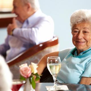 Elderly woman enjoying a social gathering with a glass of wine.