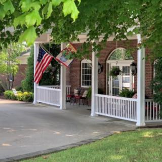 A charming house porch adorned with flags and surrounded by lush greenery.