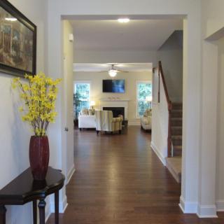 A cozy living room with hardwood floors, featuring a staircase, a television, and a vase of yellow flowers.