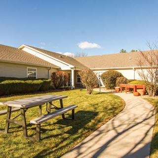 A house with a spacious yard, featuring a picnic table, pathway, and bench under a clear blue sky.