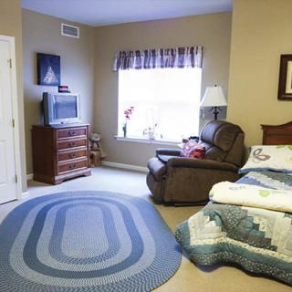 A cozy bedroom with a bed, armchair, and a TV near the window.