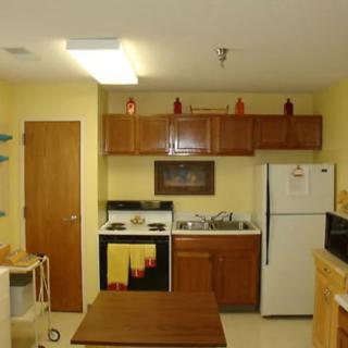 A small apartment kitchen with wooden cabinets, a refrigerator, stove, sink, and microwave.