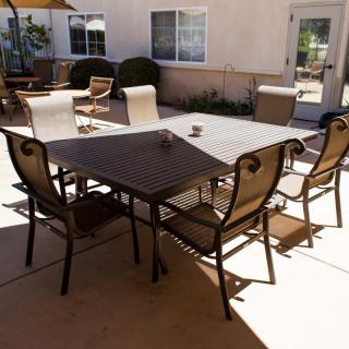 A sunny backyard patio with a table and several chairs.