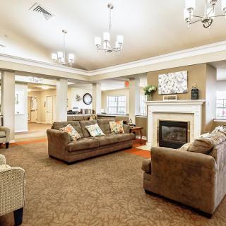 A spacious and elegantly designed living room with comfortable sofas and a fireplace, adorned by chandeliers and tasteful decor.