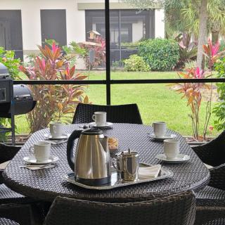 A patio setup with a table featuring coffee cups and a teapot, overlooking a garden.