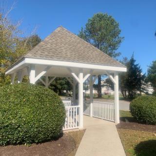 A charming white gazebo set in a landscaped garden under a clear blue sky.