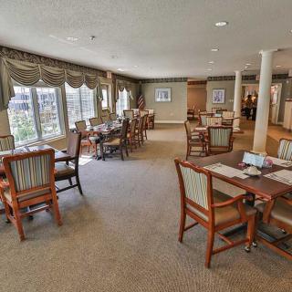 A well-lit dining area featuring multiple tables and chairs, with large windows allowing natural light to illuminate the space.