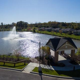A scenic view of a park with a lake, featuring a fountain and gazebo.