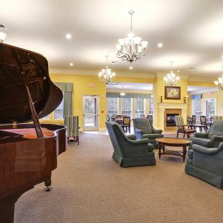 A spacious living room with a grand piano, elegant chandeliers, and cozy seating around a fireplace.