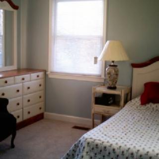 A cozy bedroom with a bed, dresser, and a lamp on a side table.