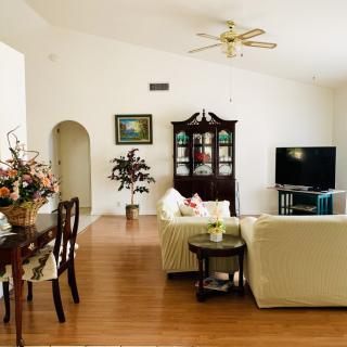 Spacious living room with a cozy seating area, adorned with elegant furniture and decor, featuring wooden floors and a ceiling fan.