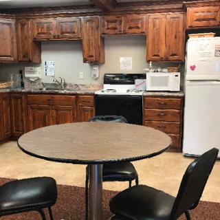 A cozy kitchen featuring a round table and black chairs, surrounded by wooden cabinets and essential appliances.