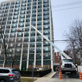 A maintenance truck positioned outside a high-rise building, equipped with an extended ladder for work on upper floors.