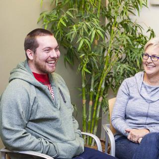 Two people sitting and enjoying a conversation indoors, surrounded by plants.