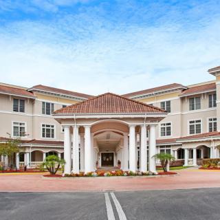 A large residential building with a grand entrance featuring columns and neatly landscaped surroundings.