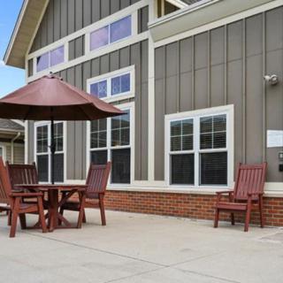 A patio with wooden outdoor furniture and an umbrella in front of a modern building exterior.