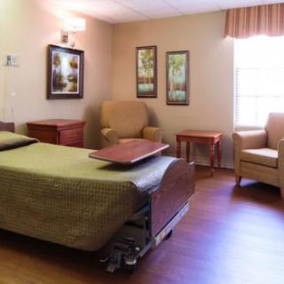 A hospital room with a patient bed, chairs, and natural light coming through the window.