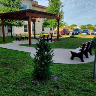 A serene outdoor garden area with benches and a pergola, surrounded by greenery.