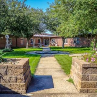 A landscaped garden pathway leading to a brick building, surrounded by lush greenery and trees.