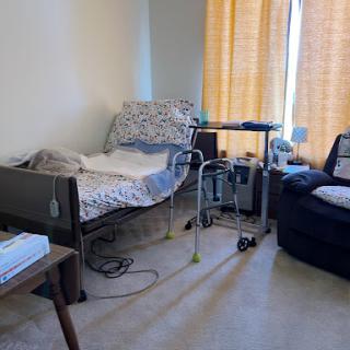 A cozy home setup featuring a hospital bed, comfortable chair, and warm yellow curtains.