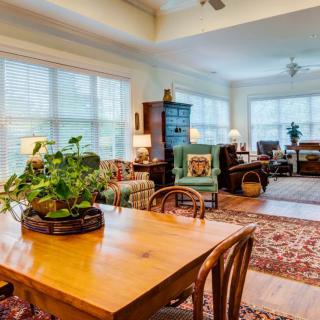 A cozy living and dining area with ample natural light, featuring wooden furniture and decorative plants.