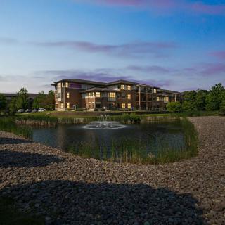 A scenic view of a residential building by a pond surrounded by greenery.