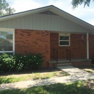 A suburban brick house with a small porch and well-maintained front yard.